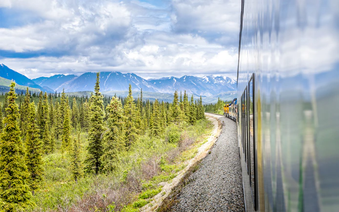 Alaska Railroad train traveling through forested mountains.
