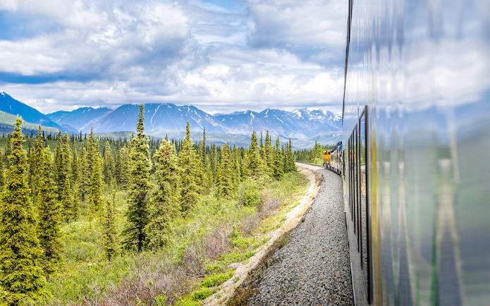 Alaska Railroad train traveling through forested mountains.