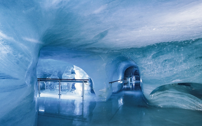 Ice tunnel at Jungfraujoch, Switzerland, with illuminated sculptures and smooth icy walls.