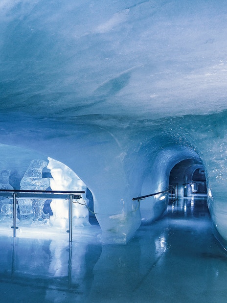 Ice tunnel at Jungfraujoch, Switzerland, with illuminated sculptures and smooth icy walls.