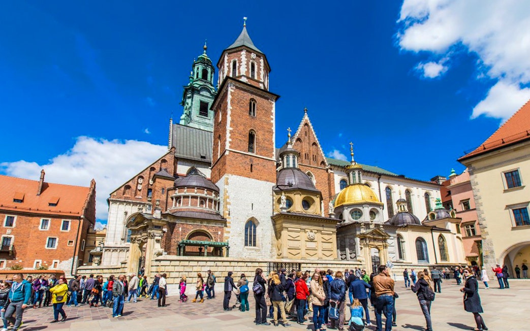Wawel Castle courtyard with tourists in Krakow, featuring cathedral domes and historic architecture.
