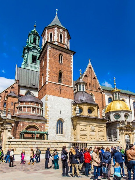 Wawel Castle courtyard with tourists in Krakow, featuring cathedral domes and historic architecture.