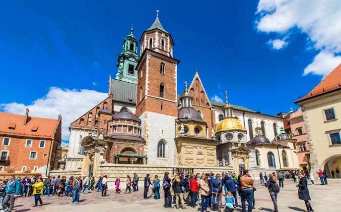 Wawel Castle courtyard with tourists in Krakow, featuring cathedral domes and historic architecture.