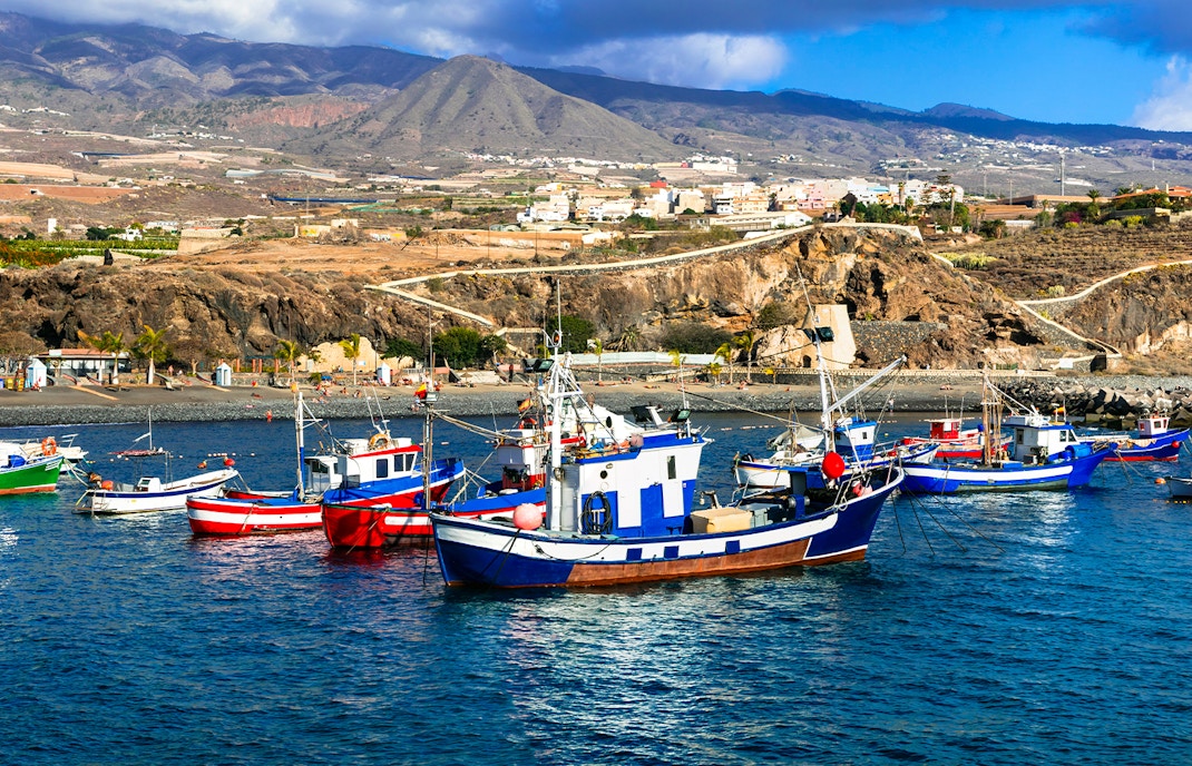 Fishing boats in Playa San Juan, Tenerife, with coastal landscape in the background.