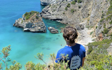 Person overlooking Ribeira do Cavalo Beach's turquoise waters and rocky cliffs near Lisbon.