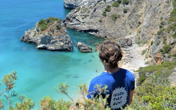 Person overlooking Ribeira do Cavalo Beach's turquoise waters and rocky cliffs near Lisbon.