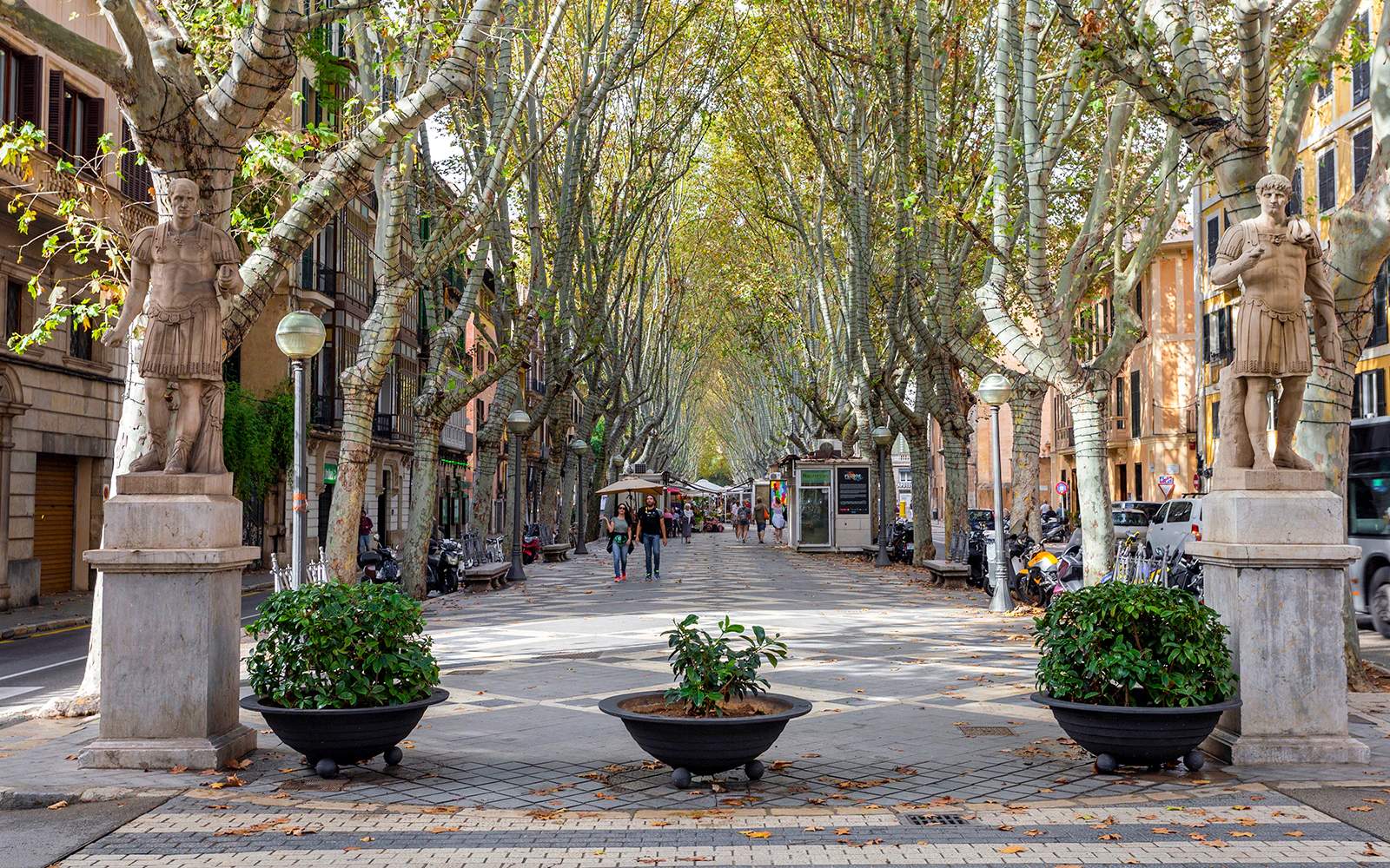 La Rambla in Mallorca lined with trees and statues, people walking along the promenade.