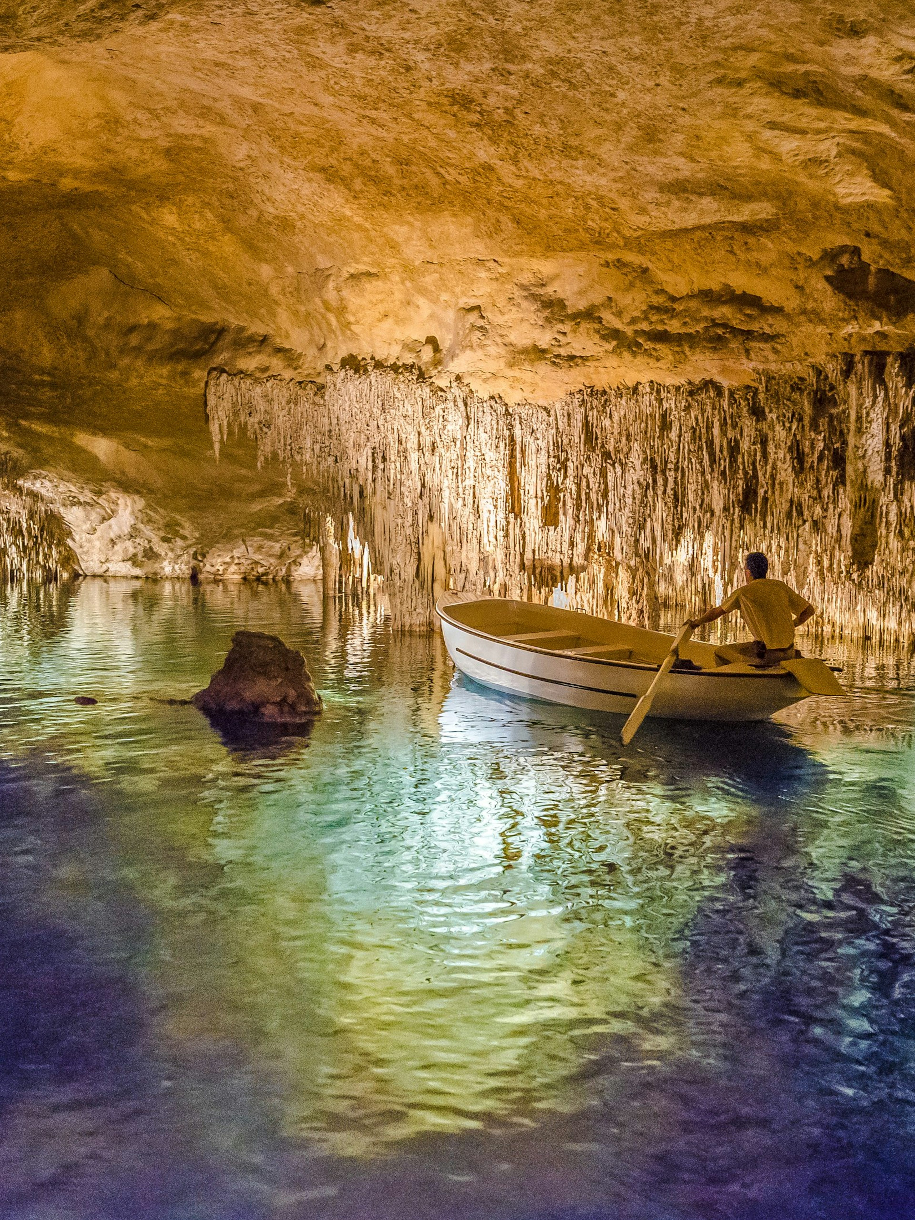 Boat tour inside Drach Caves, Majorca, with illuminated stalactites reflecting on the water.