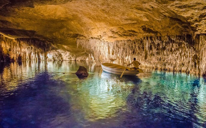 Boat tour inside Drach Caves, Majorca, with illuminated stalactites reflecting on the water.