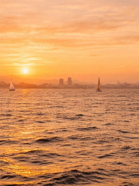 Yachts sailing at sunset with Barcelona skyline in the background.