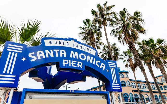 Entrance sign to the Santa Monica Pier in Santa Monica, California, with palm trees in the background.