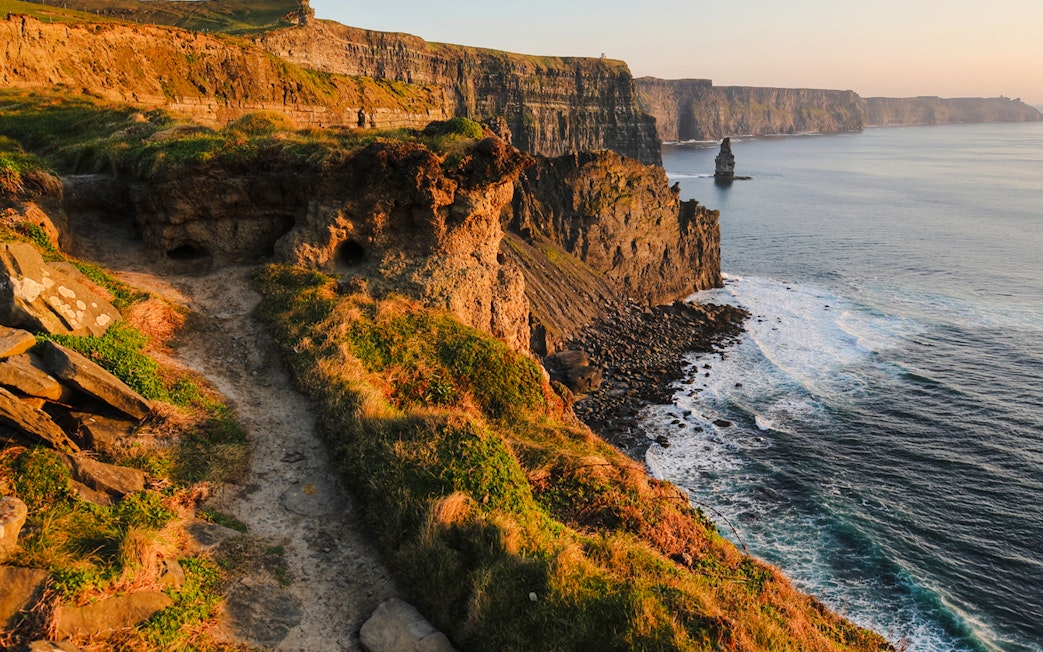 Cliffs of Moher in Ireland with ocean waves and rocky coastline at sunset.