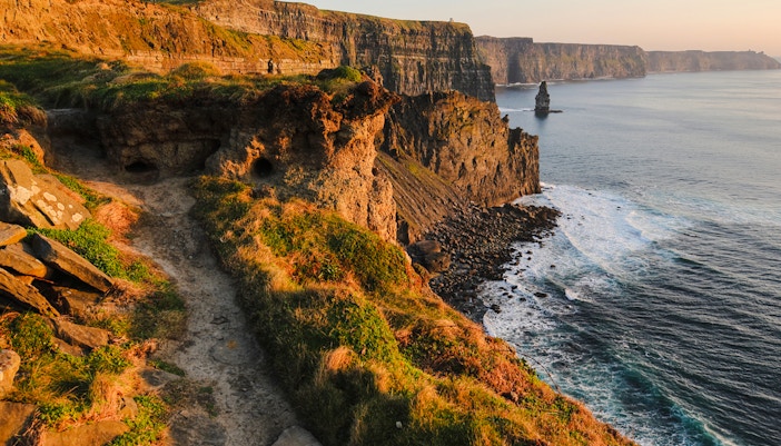 Cliffs of Moher in Ireland with ocean waves and rocky coastline at sunset.