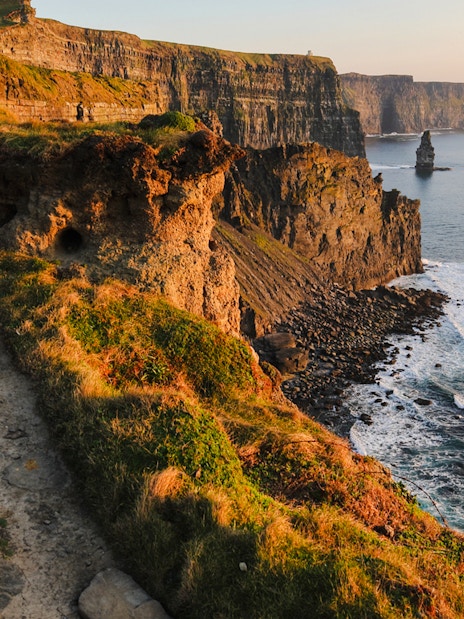 Cliffs of Moher in Ireland with ocean waves and rocky coastline at sunset.