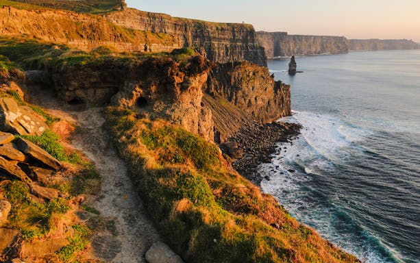 Visitors walking along the edge of the Cliffs of Moher in Ireland with the Atlantic Ocean in the background.