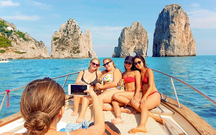 Tourists on a boat near Faraglioni rocks, Capri, during Capri & Anacapri with Blue Grotto tour.