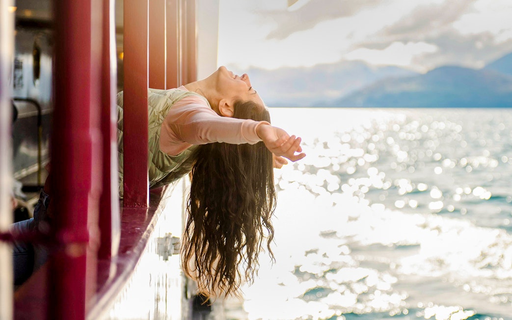 Woman leaning out steamship window with arms outstretched on a lake near Queenstown.
