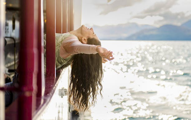 Woman leaning out steamship window with arms outstretched on a lake near Queenstown.