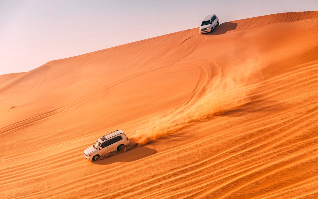 SUVs driving on sand dunes during a desert dune bashing tour in Abu Dhabi.