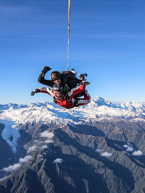 Skydivers over Franz Josef Glacier with snow-capped mountains in New Zealand.