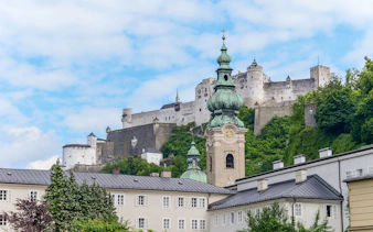 St Peters Abbey and Hohensalzburg Castle in Salzburg, Austria, with lush greenery.