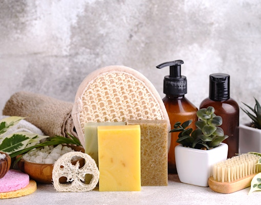 Spa essentials with natural soap bars, loofah, and skincare bottles arranged with plants.