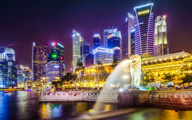 Singapore skyline with Merlion statue at night, highlighting city lights and waterfront.