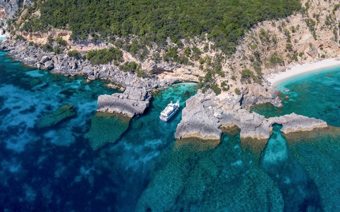 Aerial view of a boat near rocky coastline at Gulf of Orosei, Italy.