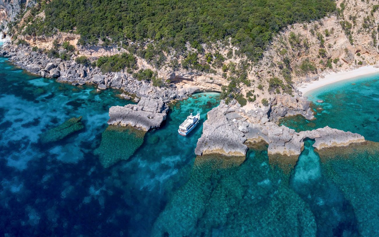 Aerial view of a boat near rocky coastline at Gulf of Orosei, Italy.