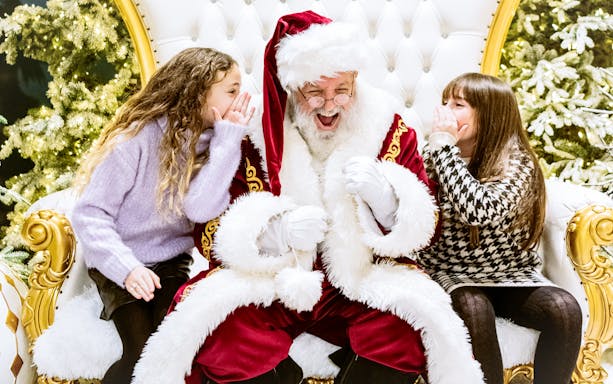 Children whispering to Santa Claus at Rockefeller Center during holiday season.