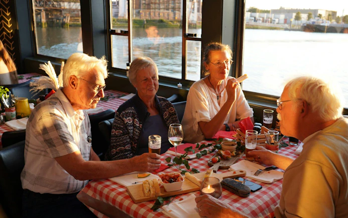 Group enjoying pizza and drinks on a river cruise at sunset.