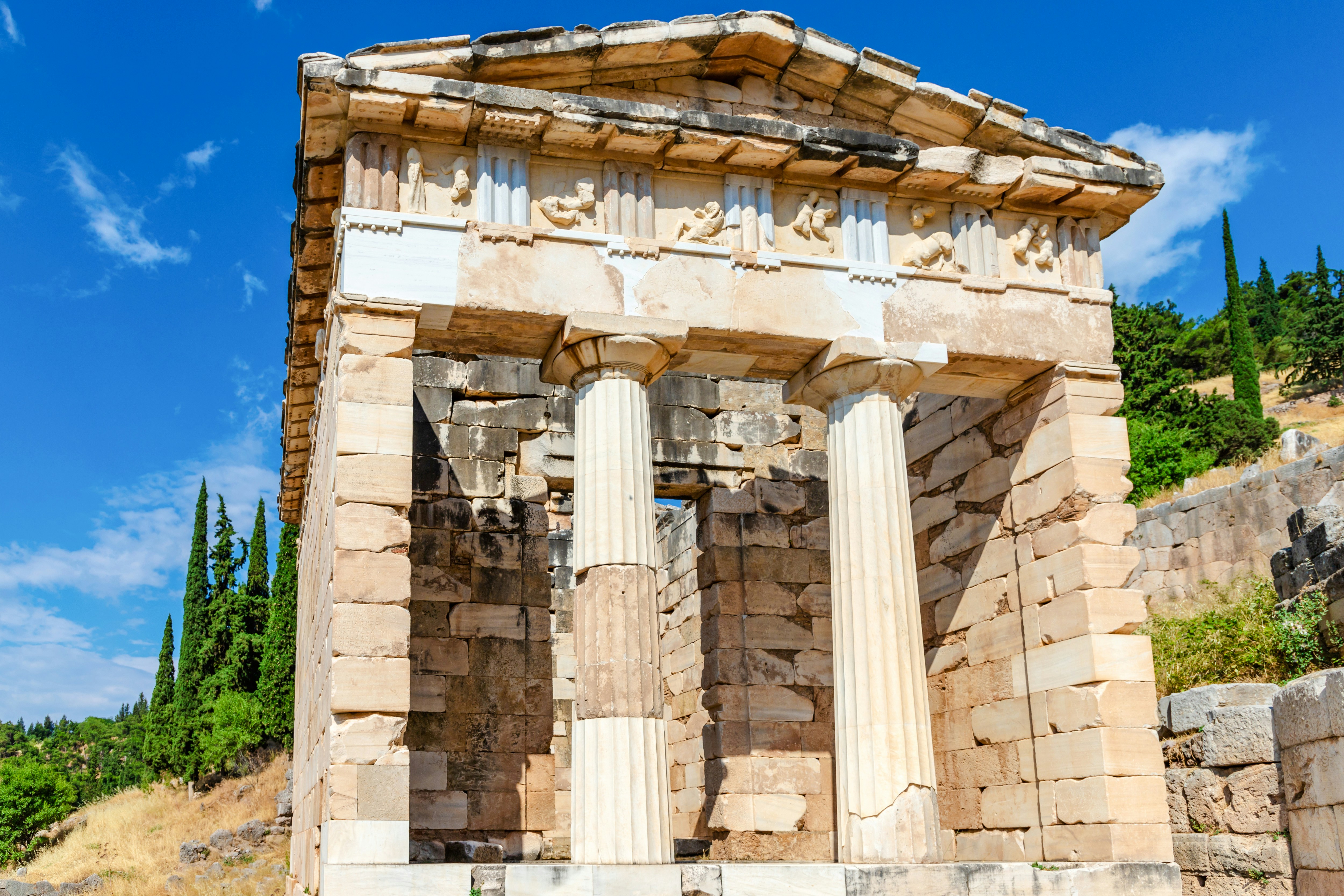 Athenian Treasury at Delphi with Doric columns and detailed frieze under a clear blue sky.