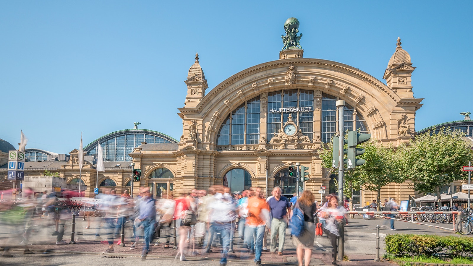 Hauptbahnhof Frankfurt train station exterior with travelers and cityscape in the background.