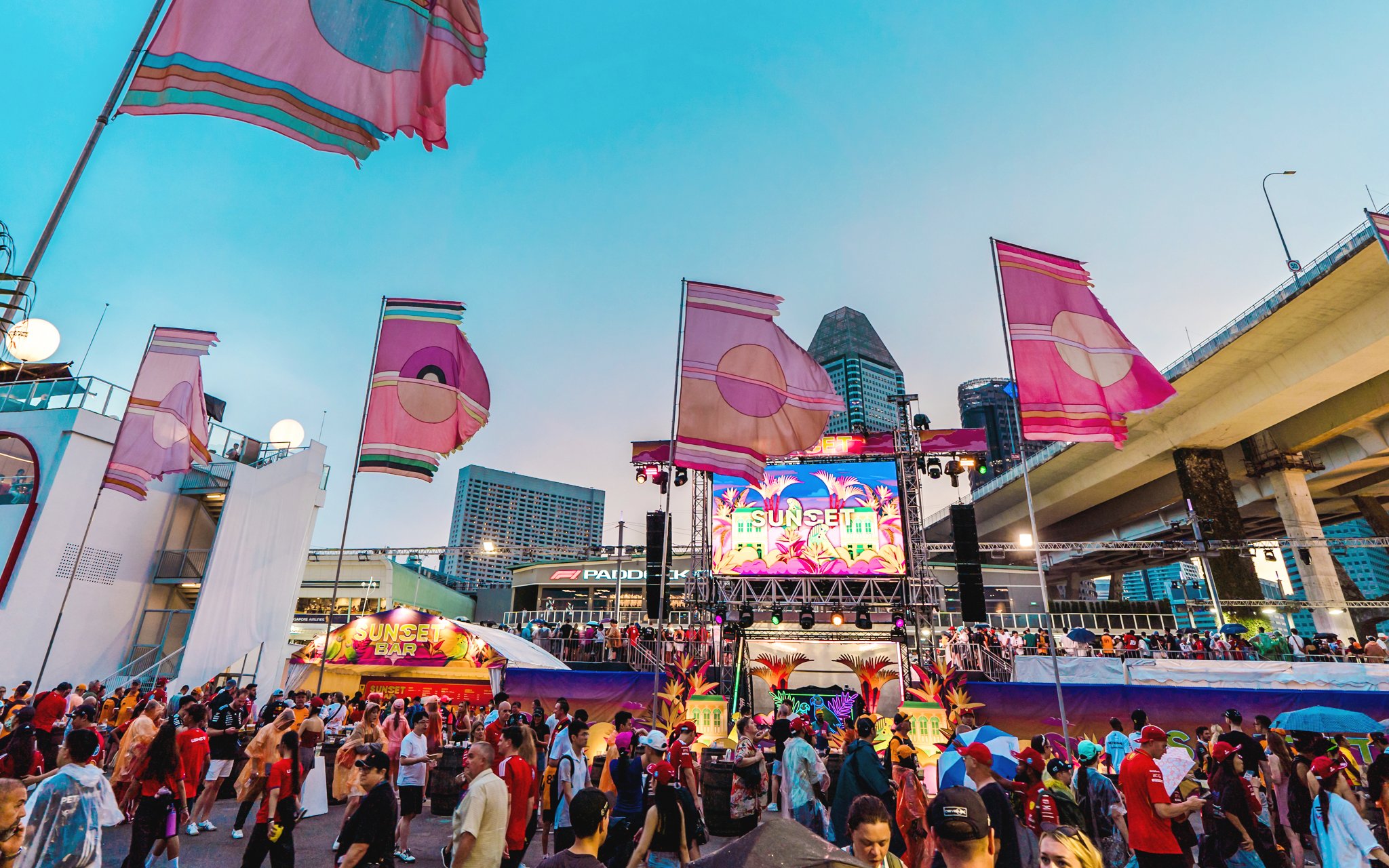Patrons enjoying the Sunset Stage in Zone 1 with colorful flags and cityscape backdrop.