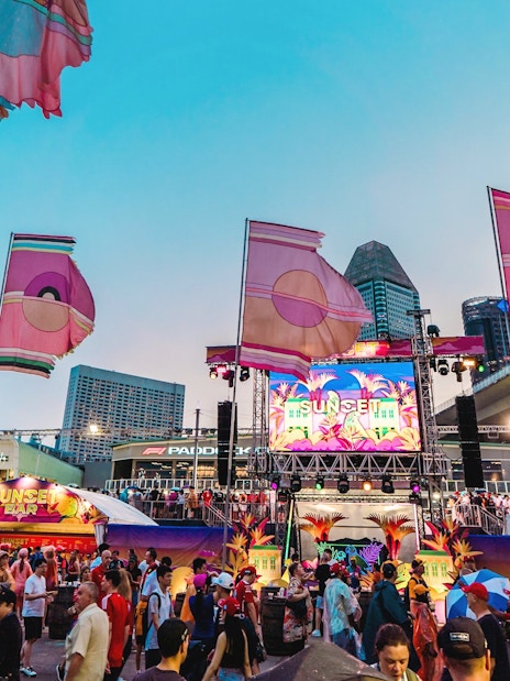 Patrons enjoying the Sunset Stage in Zone 1 with colorful flags and cityscape backdrop.