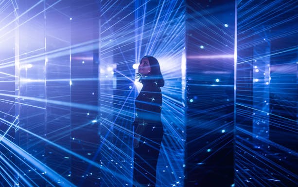 Person standing in a room with blue laser lights at ArtScience Museum's Mirror Mirror exhibit.