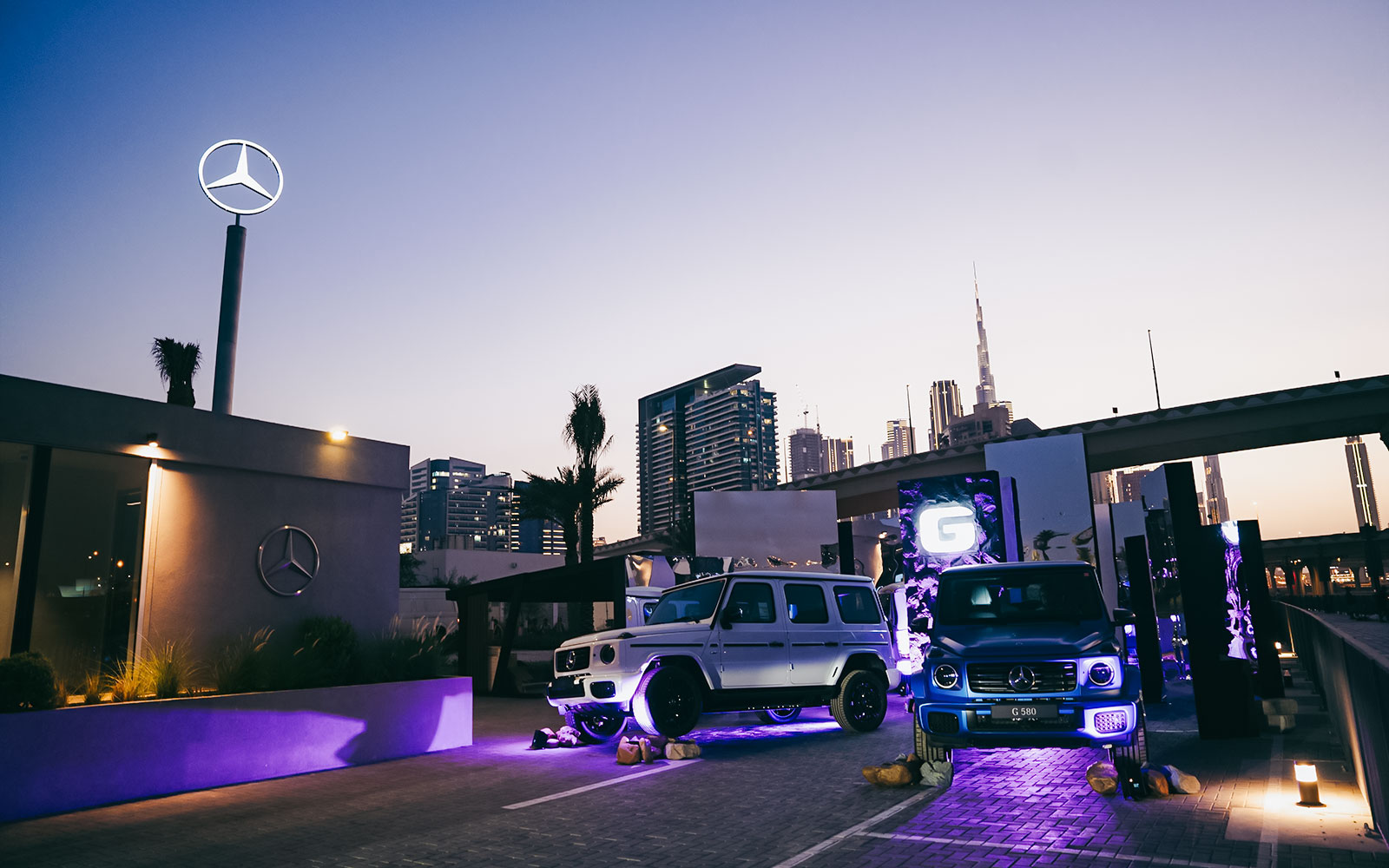 Mercedes-Benz cars illuminated at night in Dubai with city skyline in background.