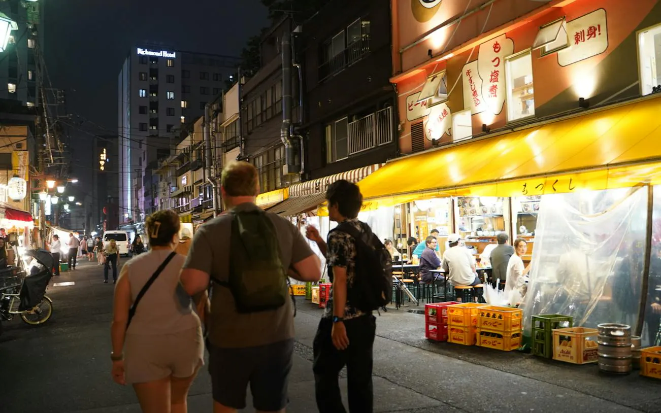 Night street scene in Asakusa, Tokyo with people walking past illuminated restaurants.