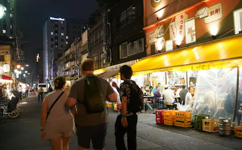 Night street scene in Asakusa, Tokyo with people walking past illuminated restaurants.