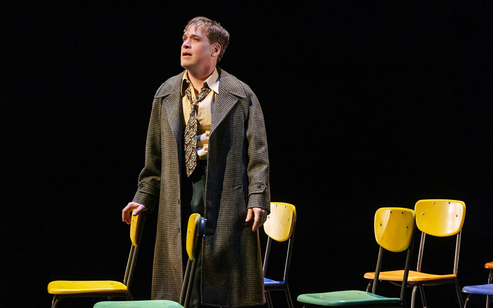 Person in a coat standing among colorful chairs on stage, Stranger Things theme.