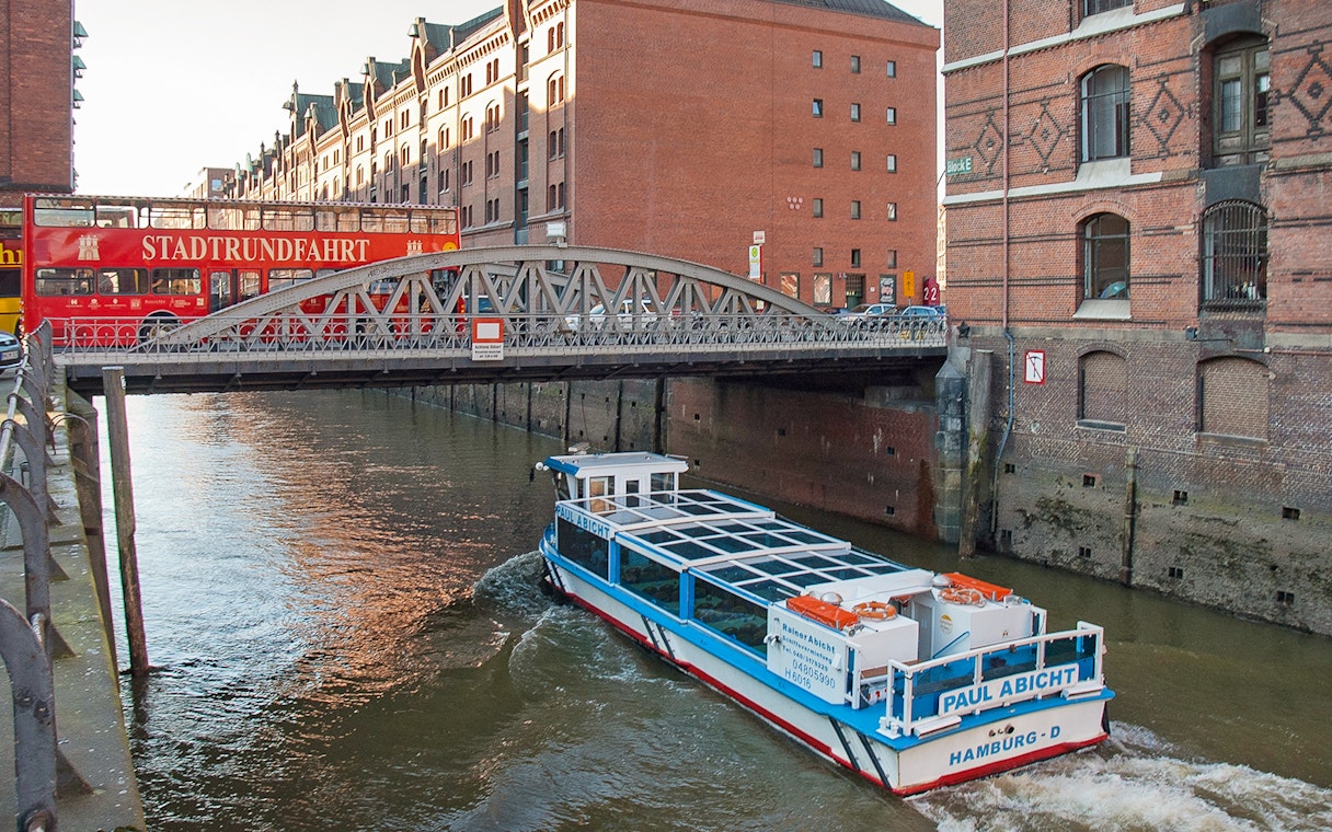 Hop-on hop-off bus and river cruise boat in Hamburg's Speicherstadt district.
