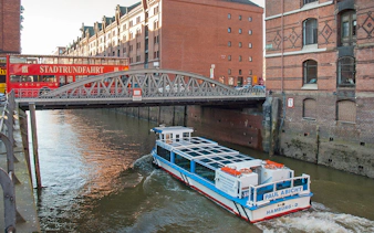 Hop-on hop-off bus and river cruise boat in Hamburg's Speicherstadt district.