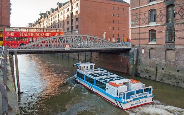 Hop-on hop-off bus and river cruise boat in Hamburg's Speicherstadt district.