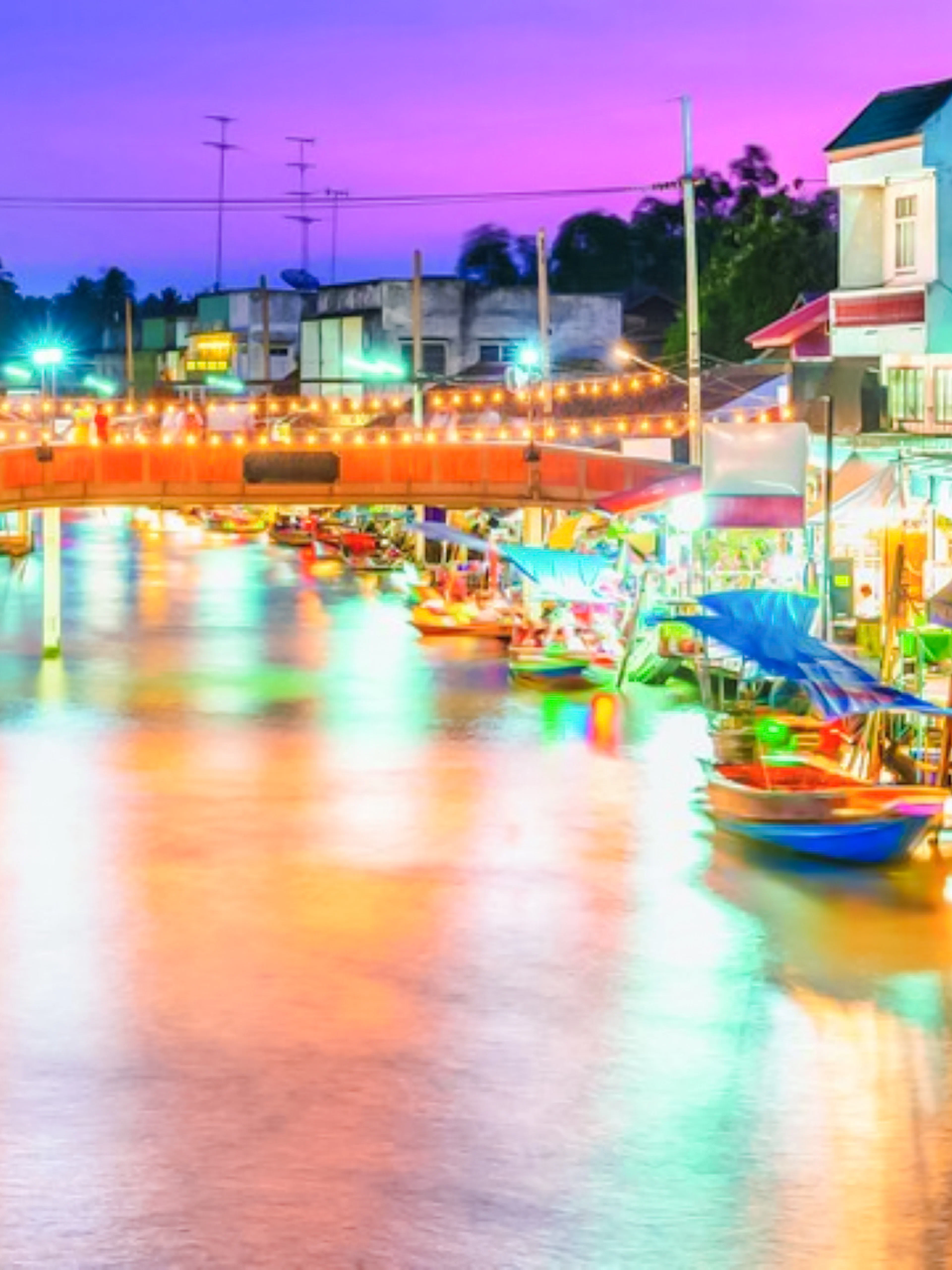 Amphawa Floating Market at night with colorful lights and boats along the canal.