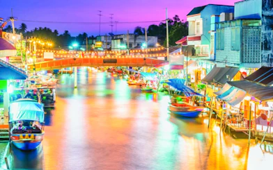 Amphawa Floating Market at night with colorful lights and boats along the canal.