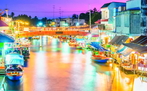 Amphawa Floating Market at night with colorful lights and boats along the canal.
