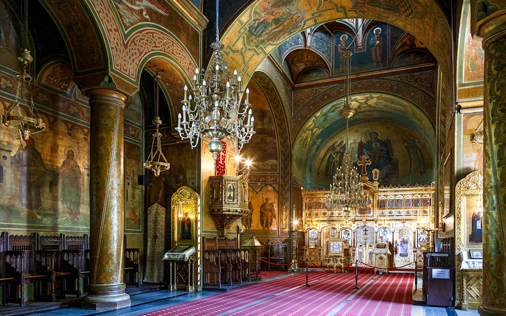 Interior of a richly decorated church with ornate chandeliers and religious frescoes, part of the Dracula's Castle day trip from Bucharest.