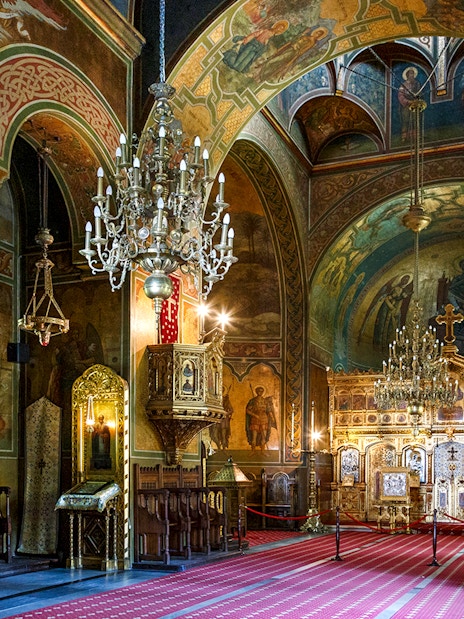 Interior of a richly decorated church with ornate chandeliers and religious frescoes, part of the Dracula's Castle day trip from Bucharest.