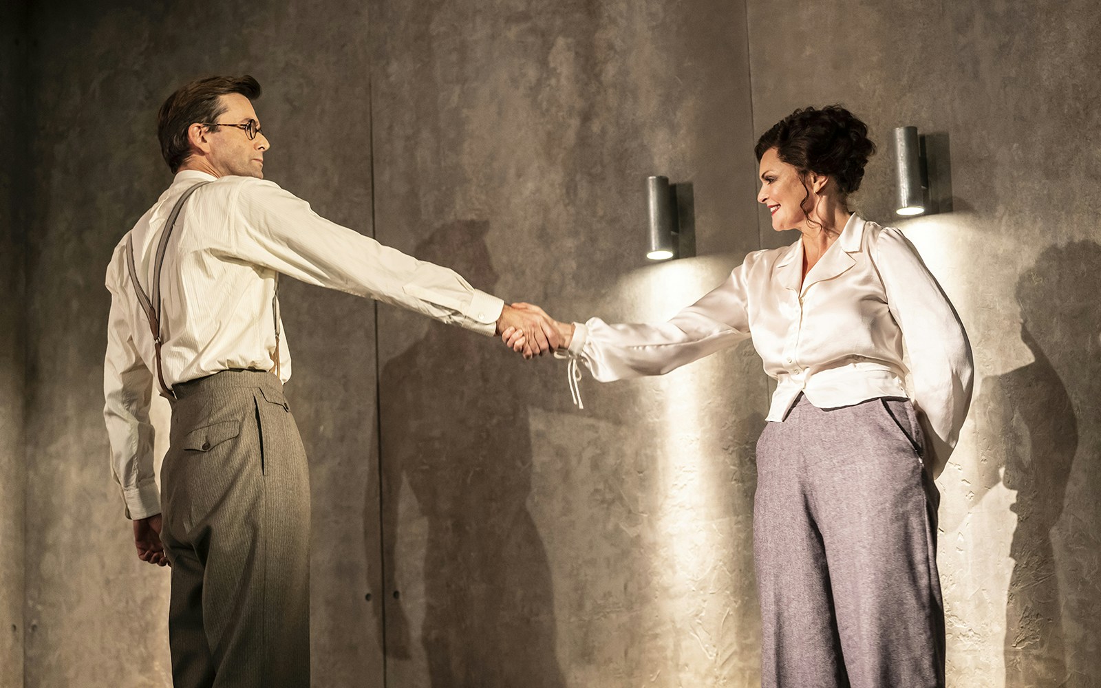 Man and woman in vintage attire shaking hands on stage.