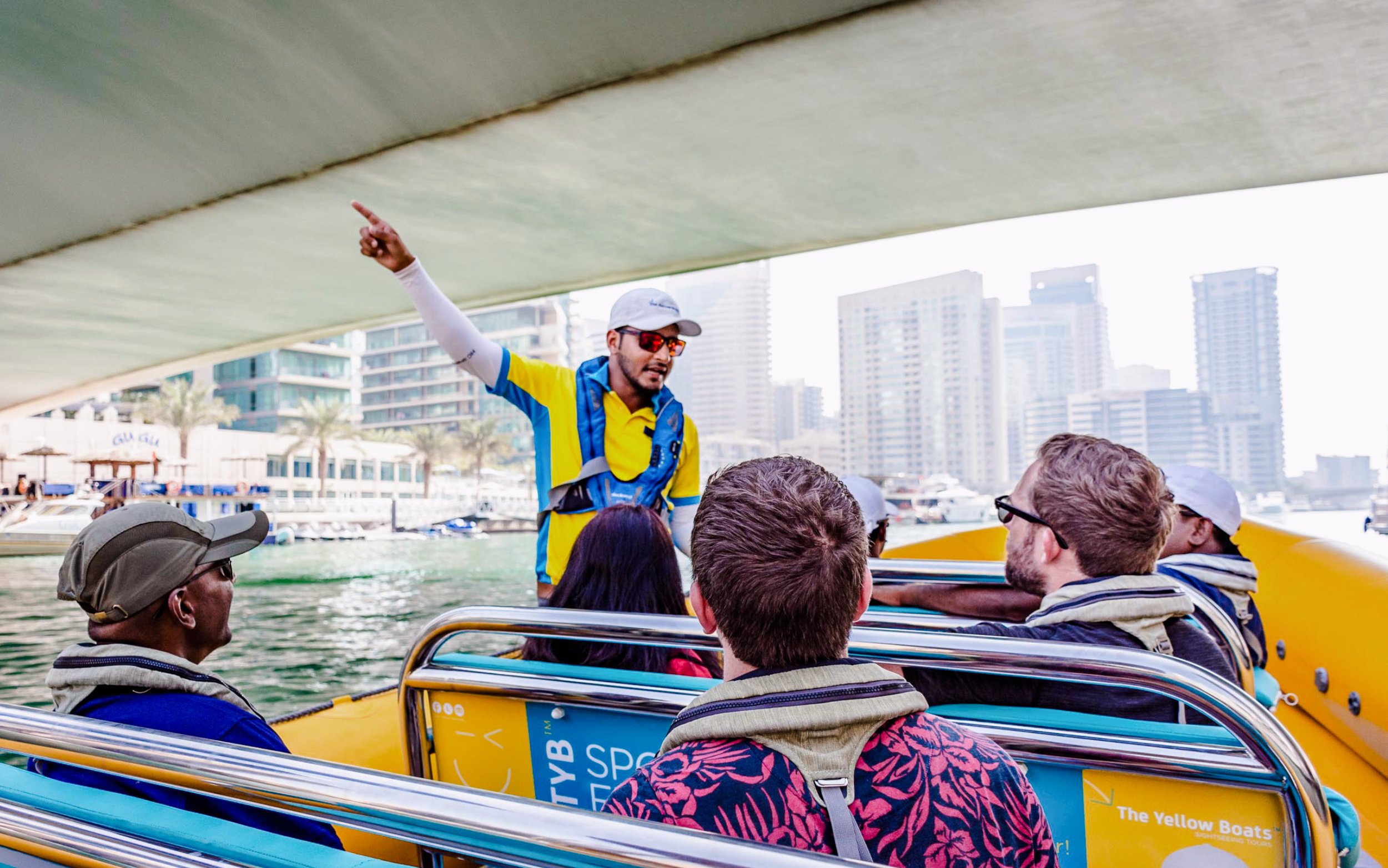 Guide pointing while interacting with tourists on a boat tour in Dubai Marina.